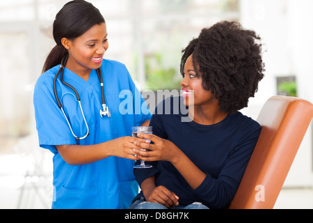 freundlichen afrikanischen Krankenschwester geben Patienten Glas Wasser in Arztpraxis Stockfoto