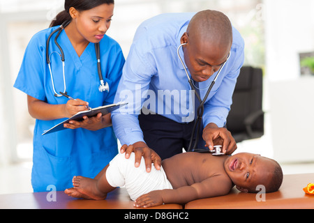 afrikanische männlichen Kinderarzt mit Schwesternassistent, die ein Kind in seinem Büro zu prüfen Stockfoto