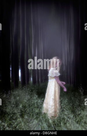 eine Mädchen in einem gelben Kleid steht in einem dunklen Wald Stockfoto