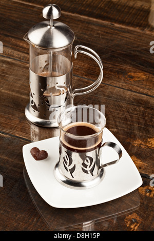 Neben einer passenden Kaffeetasse aus Glas mit Metallhülse, beide mit dekorativen Blattausschnitten. Der Becher ist gefüllt mit Stockfoto