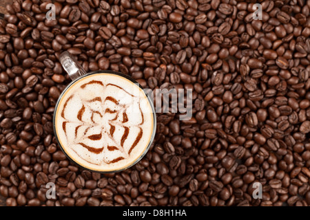 Ein Blick von oben auf eine Kaffeetasse aus Glas, gefüllt mit einem Latte mit komplizierten Latte Art in Form eines floralen oder rosenartigen Designs, hergestellt aus Kakaopulver oder Espresso auf einer Schicht Milchschaum. Die Stockfoto