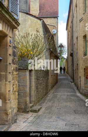 Paar geht hand in hand entlang der schmalen gepflasterten Straße unter mittelalterlichen Sandsteinbauten in charmanten Sarlat, Frankreich Stockfoto