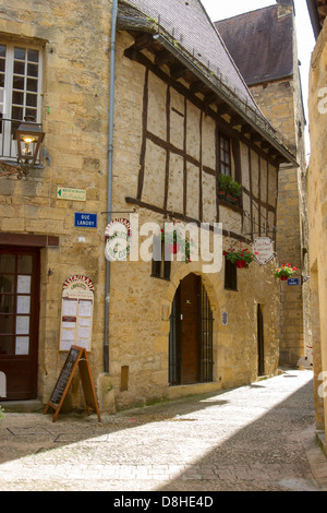Schmale gepflasterte Straße unter mittelalterlichen Sandsteinbauten gesäumt mit Geschäften in charmanten Sarlat, Dordogne Region Frankreichs Stockfoto