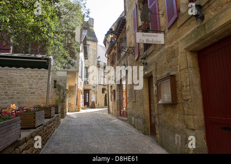 Schmale gepflasterte Straße unter mittelalterlichen Sandsteinbauten gesäumt mit Geschäften in charmanten Sarlat, Dordogne Region Frankreichs Stockfoto