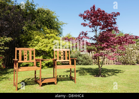 Companion Sitzbank Stühle mit einem Tisch zwischen zwei Sitzen in nachhaltigem Holz von einem Acer Baum auf einer heimischen Garten Rasen im Sommer Sonnenschein. GROSSBRITANNIEN Stockfoto