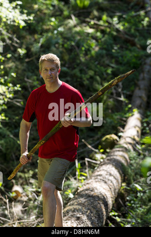 Vertikale Foto von reifer Mann Übergang über einen umgestürzten Baum halten, einen Spaziergang mit Bäumen im Hintergrund Stockfoto