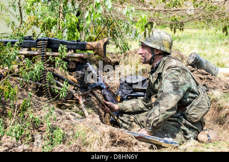 Overlord, d-Day-Re-Enactment Denmead 2013. Deutscher MG-Schütze in einem Graben hinter Tarnung versteckt. Stockfoto