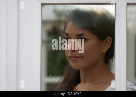 Junge Frau Blick aus Fenster Stockfoto