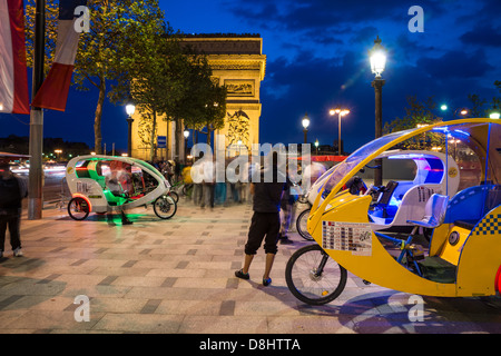 Paris, Frankreich. Velo-taxis (Velotaxis) und Cyclobulles warten in der Nähe des Arc de Triomphe als Menschen vorbei. Stockfoto