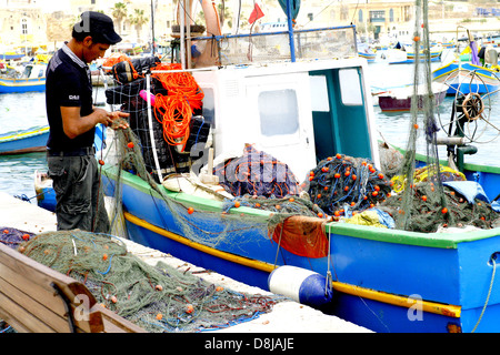 Ein Fischer seine Netze am Kai in Marsaxlokk, Malta zu überprüfen. Stockfoto