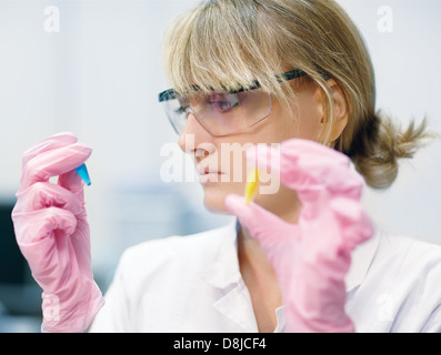 niedrigen Schwerpunkt Porträt der jungen Wissenschaftlerin Schutzbrille und Handschuhe vergleicht zwei Reagenzgläser Stockfoto