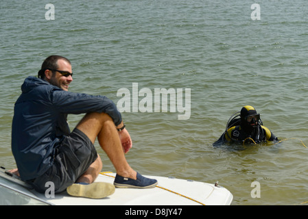 Einige Männer, man sitzt auf einem Motorboot lächelnd mit einem Taucher im Wasser Stockfoto