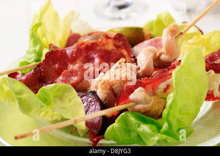 Hähnchen-Spieße und Speckstreifen, serviert auf Salatblättern Stockfoto