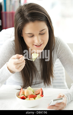 Porträt einer jungen Frau Obstsalat zu essen, während des Surfens mit ihrem iphone Stockfoto