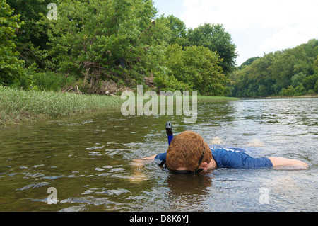 Ein Schnorchler taucht in einen flachen Fluss ein und erkundet die Unterwasserwelt. Das klare Wasser bietet hervorragende Sicht, sodass der Taucher die Wasserwelt aus nächster Nähe beobachten kann. Flache Flüsse beherbergen oft eine Vielzahl von Fischen und Pflanzen, was ein friedliches und immersives Erlebnis für diejenigen bietet, die die Natur unter der Oberfläche erkunden möchten. Stockfoto