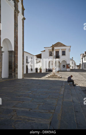 Ein älterer Mann sitzt auf der Treppe in einem sehr schönen Platz vor einer Kirche in Monasaraz.  Alentejo, Portugal. Stockfoto