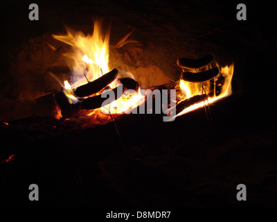 Hot Dogs werden auf Stöcken über einem offenen Lagerfeuer gekocht, Teil eines klassischen Camping-Erlebnisses im Freien. Stockfoto