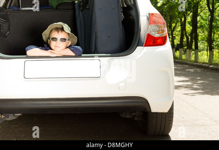 Verspielte junge Verlegung in den LKW eines weißen Schrägheck-Autos und Ausschau, moderne Sonnenbrille und einen Hut tragen Stockfoto