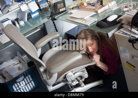 Frau versteckt unter einem Schreibtisch. Stockfoto