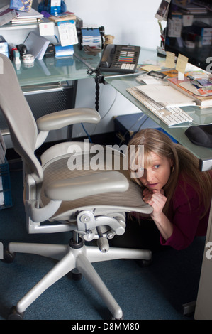 Frau, verstecken und spähen aus unter ihrem Schreibtisch. Stockfoto