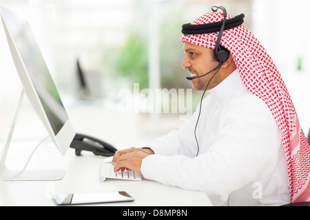 lächelnd nahöstlichen Geschäftsmann arbeiten auf einem Computer mit Kopfhörer Stockfoto