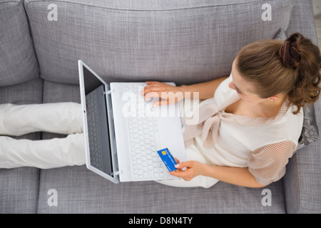 Junge Frau, die Verlegung auf Sofa mit Laptop und Kreditkarte Stockfoto