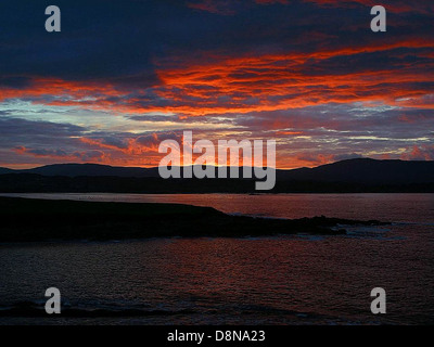 Eine atemberaubende Landschaft bei Sonnenuntergang, bei der die Sonne unter den Horizont fällt und ein warmes orangefarbenes Leuchten über den Himmel wirft. Die Szene ist friedlich mit minimaler Wolkendeckung und einem ruhigen Horizont. Stockfoto