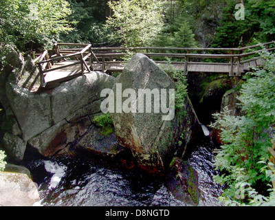 Dieses Bild zeigt eine Holzbrücke in einer bergigen Landschaft, die zum Überqueren von Bächen oder Schluchten bestimmt ist. Holzbrücken sind in natürlichen Umgebungen üblich und bieten eine langlebige und zugleich ästhetisch ansprechende Struktur, die sich mit der Umwelt verbindet. Stockfoto