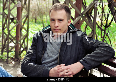 Hübscher junger Mann sitzt auf einer Bank in einem Park. Stockfoto