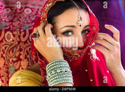 Schöne, geheimnisvolle Frau in roten bestickten indischen Hochzeit Sari und traditionellen Schmuck mit Gesicht bedeckt teilweise Stockfoto