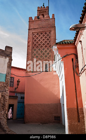Frau in der Tür unter dekorativen arabischen Minarett, bunte Gebäude mit blauem Himmel, Marrakesch, Marokko Stockfoto