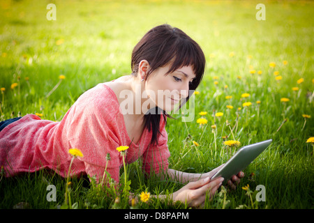 Junge Frau mit Tablet im Freien auf dem Rasen verlegen Stockfoto