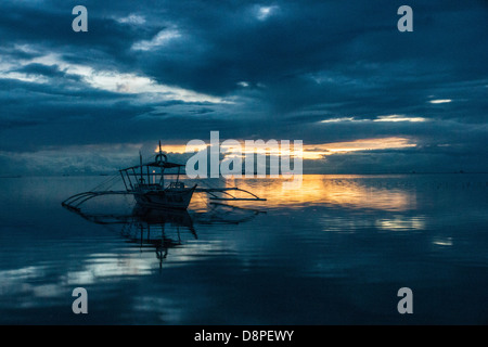 Vertäut Ausleger Bangka - einem traditionellen philippinischen Fischerboot - mit Leuchtturm Strahlen in den Sonnenuntergang Stockfoto