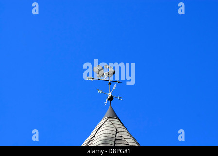 Wetterfahne Hahn mit Himmelsrichtungen und Pfeil am strahlend blauen Himmel. Stockfoto