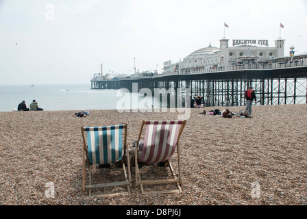 Zwei Liegestühle am Strand von Brighton, Brighton, England, mit Brighton Pier im Hintergrund. Stockfoto