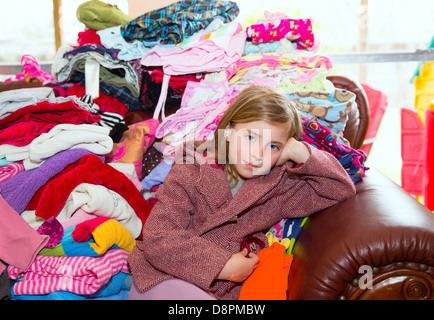 Blondes Kind Mädchen sitzen auf einem Sofa unordentliche Kleidung Spielbetrieb Wäsche Stockfoto