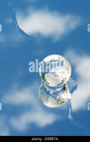 Kristall Glas Globus / Erde / Welt auf einem Spiegel mit Wasser reflektieren blaue Himmel Stockfoto