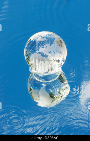 Kristall Glas Globus / Erde / Welt auf einem Spiegel mit Wasser reflektieren blaue Himmel Stockfoto