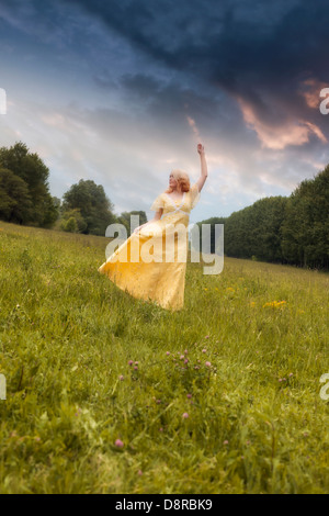 eine Mädchen in einem gelben Kleid tanzt auf einer Wiese Stockfoto