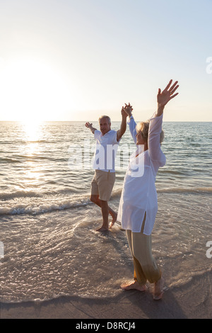 Glückliches Paar der senior Mann und Frau zu Fuß und Hand in Hand auf einem einsamen tropischen Strand mit strahlend blauem Himmel Stockfoto
