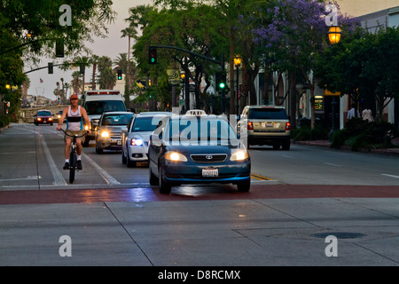 State Street in Santa Barbara, Kalifornien, die Autos mit Scheinwerfern auf Radfahrer und Fußgänger in der Abenddämmerung aufgenommen. Stockfoto