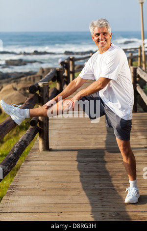 aktive reifer Mann Dehnung Bein am Strand am Morgen Stockfoto