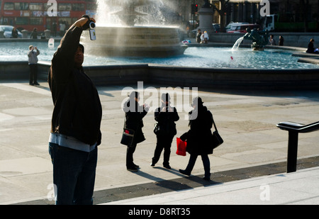 Touristen fotografieren auf dem Londoner Trafalgar Square mit Brunnen im Hintergrund Stockfoto