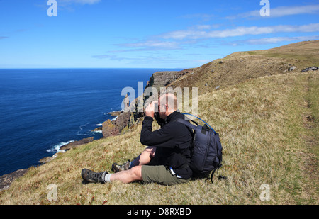 Mann, Blick auf das Meer durch ein Fernglas mit der Greis Stoner im Hintergrund in Sutherland Schottland Stockfoto