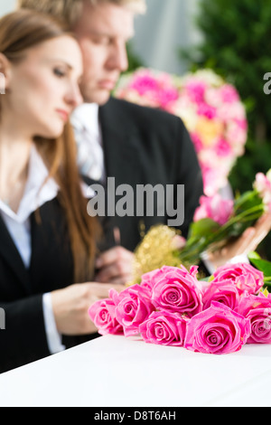 Trauer um Mann und Frau auf der Trauerfeier am Sarg oder Sarg mit rosa rose Stockfoto