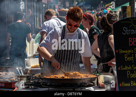 Koch Kochen einen Topf mit Paella und und ein Grill der Hamburger auf ein Outdoor-Kocher Stockfoto