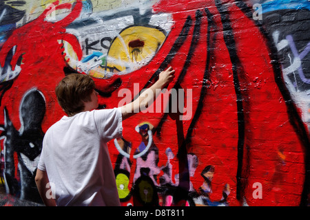 Youngster mit Spray kann in Gasse sprühen bunte Graffiti an der Wand des Gebäudes in der Stadt Stockfoto