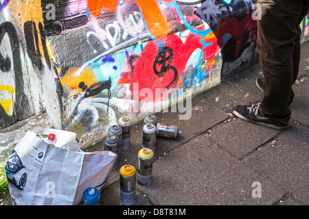 Spraydosen auf dem Boden und Youngster sprühen bunte Graffiti an der Wand des Gebäudes in der Stadt Stockfoto