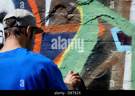 Youngster mit Spray kann in Gasse sprühen bunte Graffiti an der Wand des Gebäudes in der Stadt Stockfoto