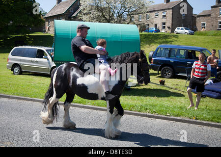 Zigeunerreisende in Bainbridge, Richmondshire, North Yorkshire, Großbritannien Juni, 2013. Vater und cvhild zu Pferd als Mitglieder der Wandergemeinschaft reisen auf dem Weg zur Appleby Horse Fair in Cumbria. Die Messe ist ein jährliches Treffen von Zigeunern und Reisenden, das in der ersten Juniwoche stattfindet und seit der Regierungszeit von James II. Stattfindet, der 1685 eine königliche Charta für eine Pferdemesse in der Nähe des Flusses Eden erteilte. Stockfoto